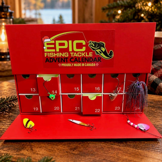 A red 24-day fishing tackle advent calendar displayed on a wooden table in a festive indoor setting. The calendar features numbered compartments with various fishing lures and hooks, and the front lid is printed with 'EPIC FISHING TACKLE ADVENT CALENDAR' and a fish graphic.